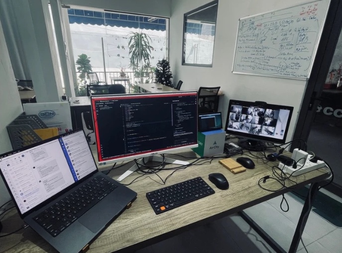 A desk with a laptop, a monitor showing code, an AirCity box and a camera feed screen