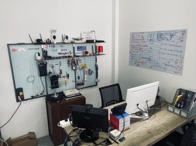 A pegboard of devices and tools under partner logos, next to a whiteboard full of diagrams